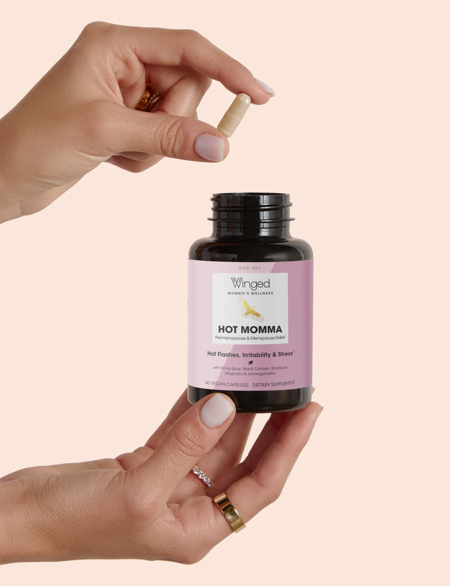 A woman holding a single Winged Wellness Hot Momma Menopause Support Supplement capsule over the bottle