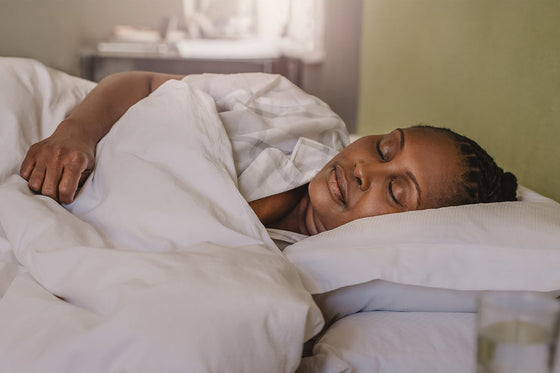 An African American woman sleeping soundly on her side under a white comforter, highlighting the potential for restful sleep during menopause