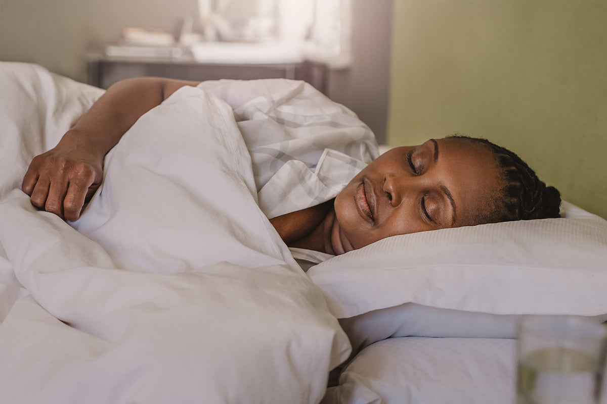 An African American woman sleeping soundly on her side under a white comforter, highlighting the potential for restful sleep during menopause