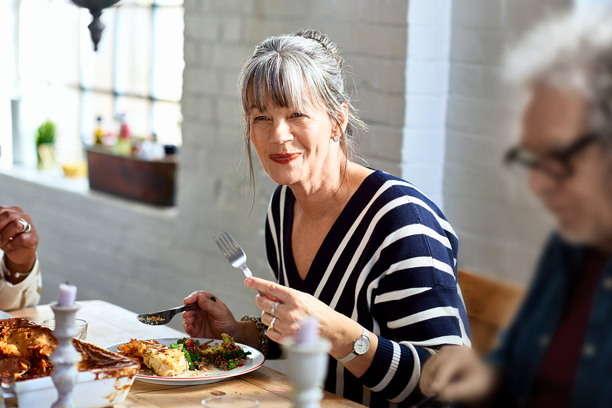 Older woman with gray hair enjoying a heart-healthy meal at home, highlighting dietary choices that support cholesterol management during menopause