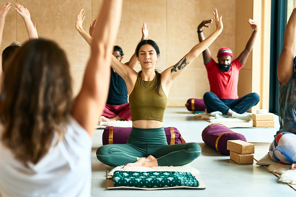 A woman leads a yoga class, demonstrating a calming pose that may help relieve symptoms of menopause and perimenopause. The class is diverse and supportive, showing yoga's accessibility.