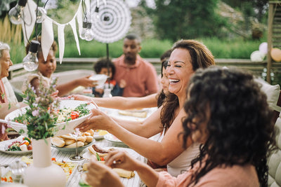 A group of people sharing a Mediterranean-style meal outdoors, featuring fresh salad, vegetables, whole grains, and olive oil, illustrating healthy eating habits that support women during perimenopause.