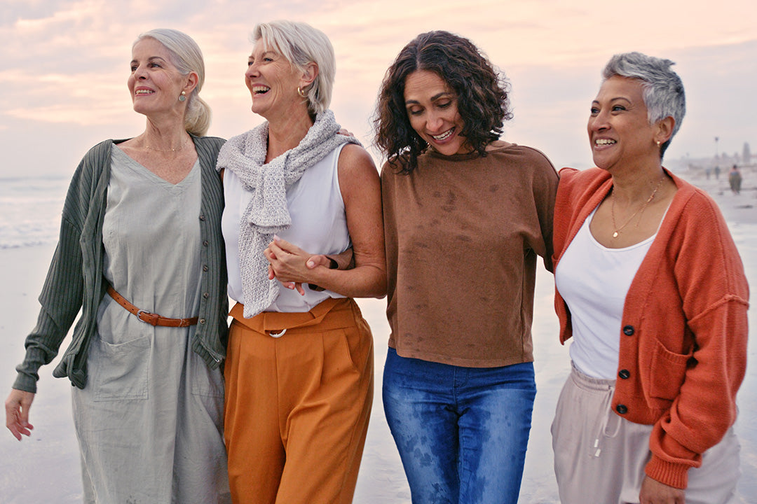 A group of four friends, representing the vitality and connection possible during and after menopause, walking together on a beach at sunset.