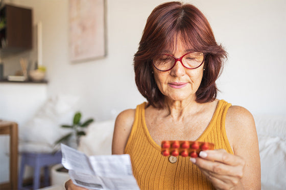 a mature woman wearing an ochre-colored top examines a package insert while holding a blister pack of hormone therapy pills
