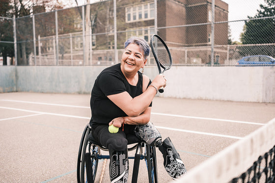 A person using a wheelchair who has prosthetic legs plays tennis outdoors, showing active movement and exercise as an important part of managing postmenopausal symptoms.