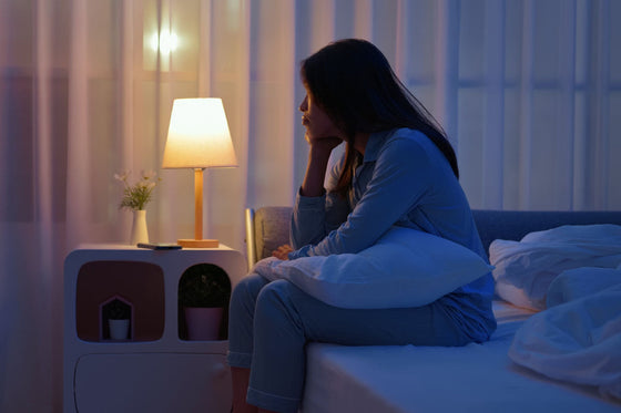 Woman in perimenopause sitting on a bed at night in a dimly lit bedroom experiencing menopause-related sleep issues