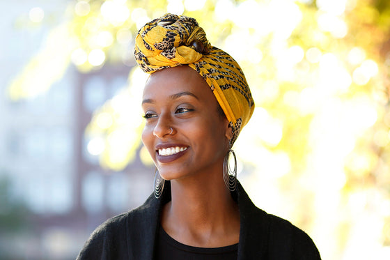 A smiling Black woman wearing a vibrant headwrap, representing the strength and beauty of women experiencing menopause