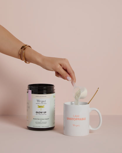 A woman's hand pouring Winged Wellness Glow Up Collagen & Stress Drink Mix Powder into a coffee mug